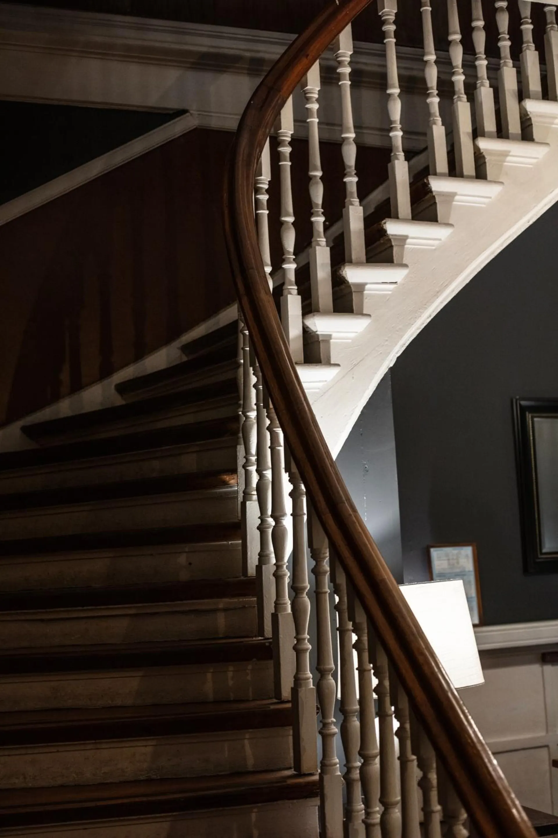 La escalera de madera de la casona, con barandas torneadas que suben en curva entre muros oscuros.